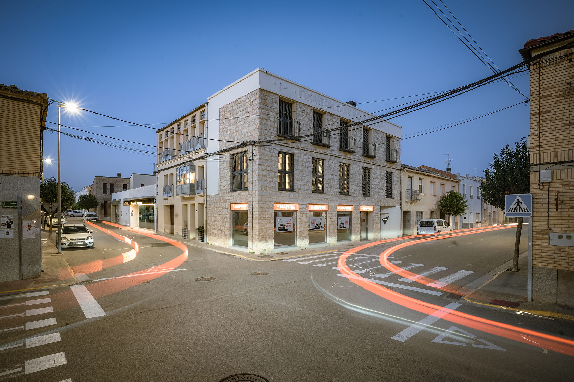 Vista nocturna de la fachada del edificio de oficinas Mapfre en esquina con estelas de luz de coches